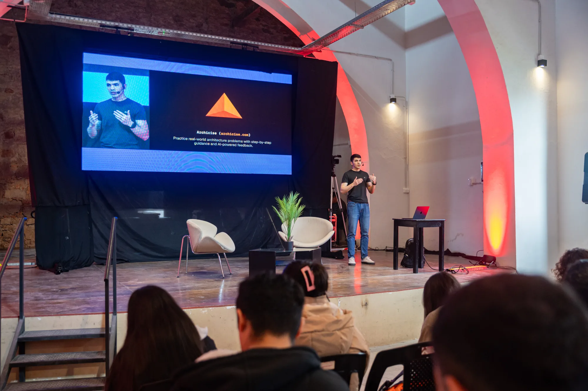 Agustín Sánchez giving a talk on stage, next to a slide reading "Agentic Software".