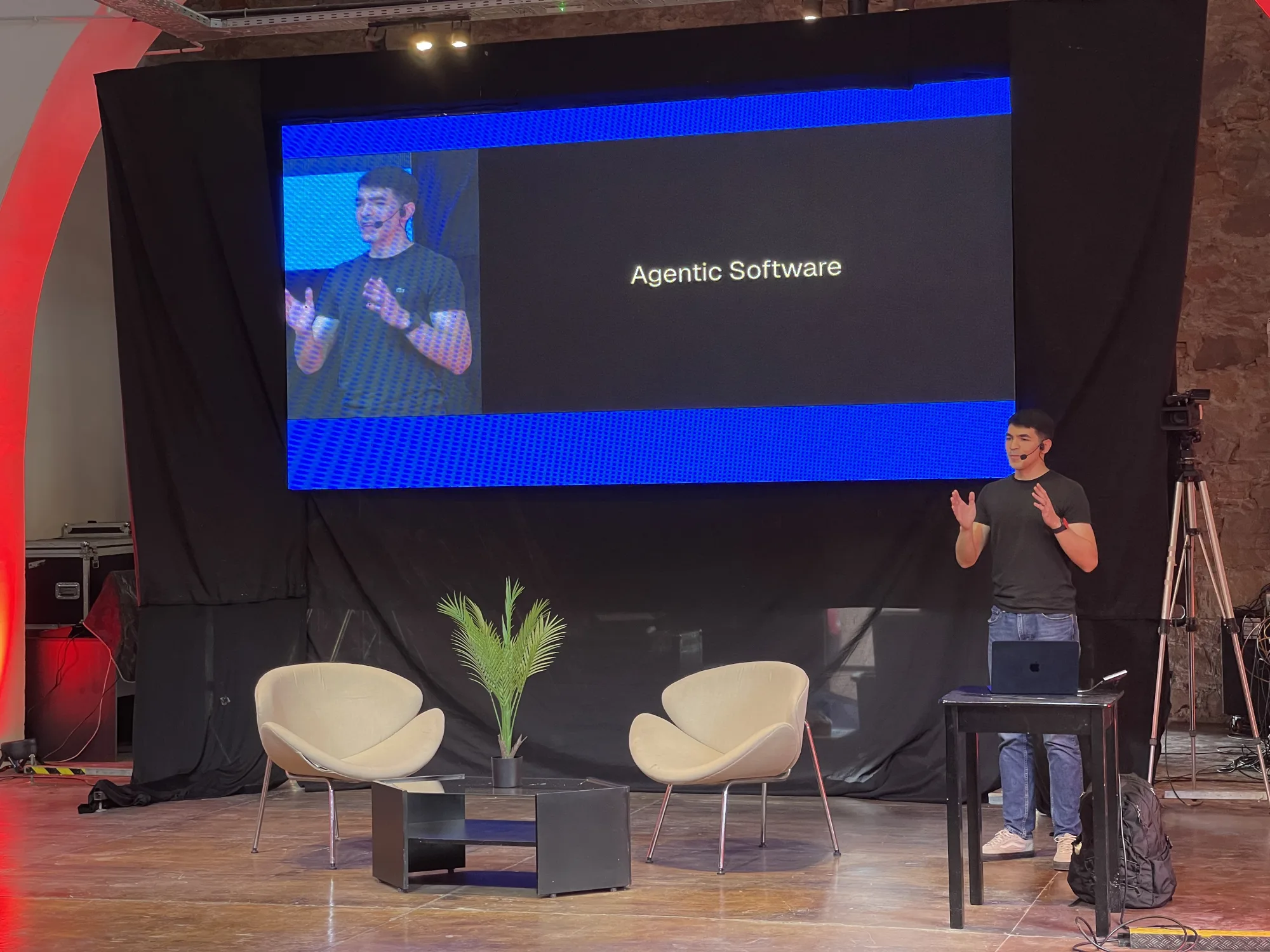 Agustín Sánchez giving a talk on stage, next to a slide reading "Agentic Software".